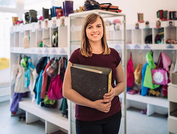 Young woman with file folder in front of the cloakroom of a day-care centre