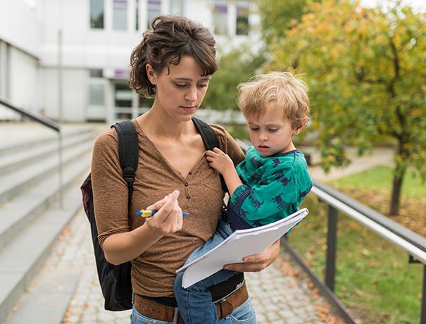 Student with child in her arms and writing pad in hand