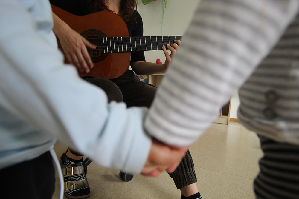 Gitarrenspiel und Kinder, die sich an den Händen fassen